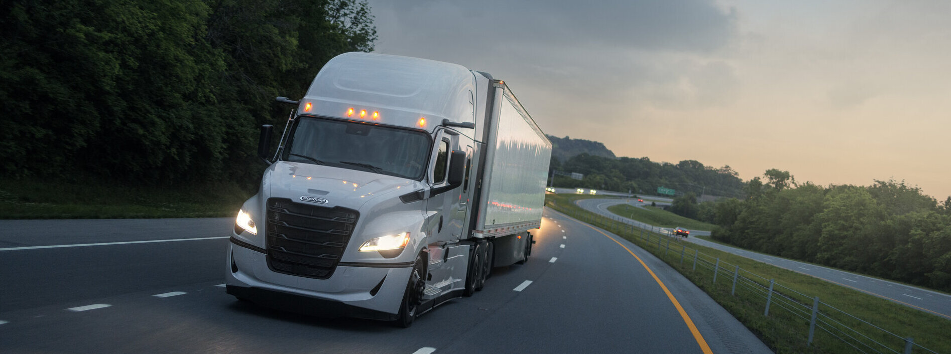 A white semi truck with a plain, unbranded trailer on the highway at dusk